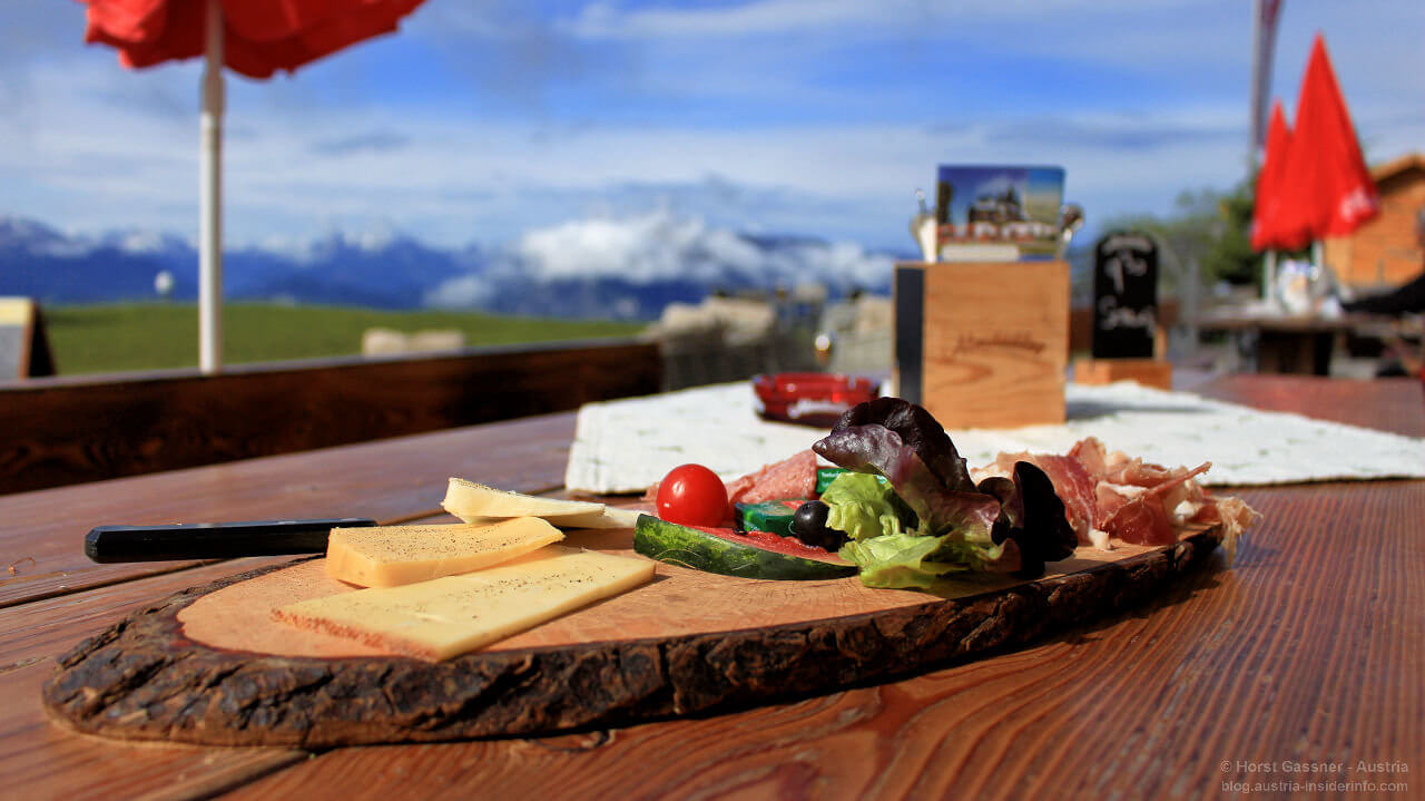 Speisen auf einem Holzbrett mit Ausblick über Berge